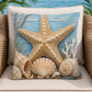 A square decorative throw pillow with a beach-themed print featuring a large starfish, seashells, and coral on a blue wood-plank background, displayed on a beige outdoor chair.