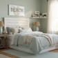 Neatly made bed in a bedroom with decorative elements and a 'BEACH' sign on the wall.