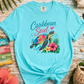 Turquoise t-shirt with a turtle graphic and 'Caribbean Soul' text on a wooden surface with tropical decorations.