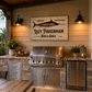 Outdoor kitchen with 'Lazy Fisherman Bar & Grill' sign, grill, and refrigerator.