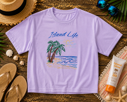 Purple t-shirt with 'Island Life' design on a wooden surface with beach accessories.