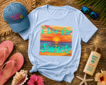 Light blue t-shirt with sunset design and 'Beach Life' cap on a wooden surface with flip-flops and sunscreen.
