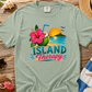 Light green t-shirt with 'Island Therapy' design on a wooden surface with beach-themed items.