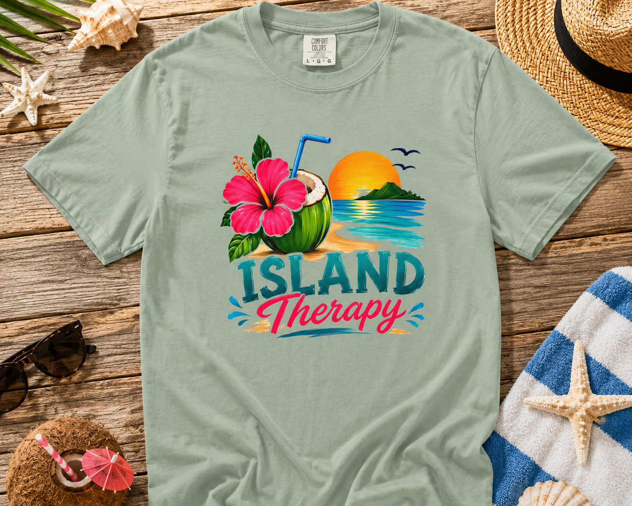 Light green t-shirt with 'Island Therapy' design on a wooden surface with beach-themed items.