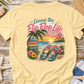 Beige t-shirt with 'Living the Flip Flop Life' graphic on a wooden surface with beach accessories.