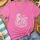 A pink V-neck t-shirt with a white 'Ocean Life' seahorse graphic, styled in a flat lay with denim shorts, a straw hat, sunglasses, flip-flops, and beach accessories on a wooden surface.