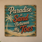 Decorative sign with 'Paradise is Sand Between My Toes' text on a wooden background.