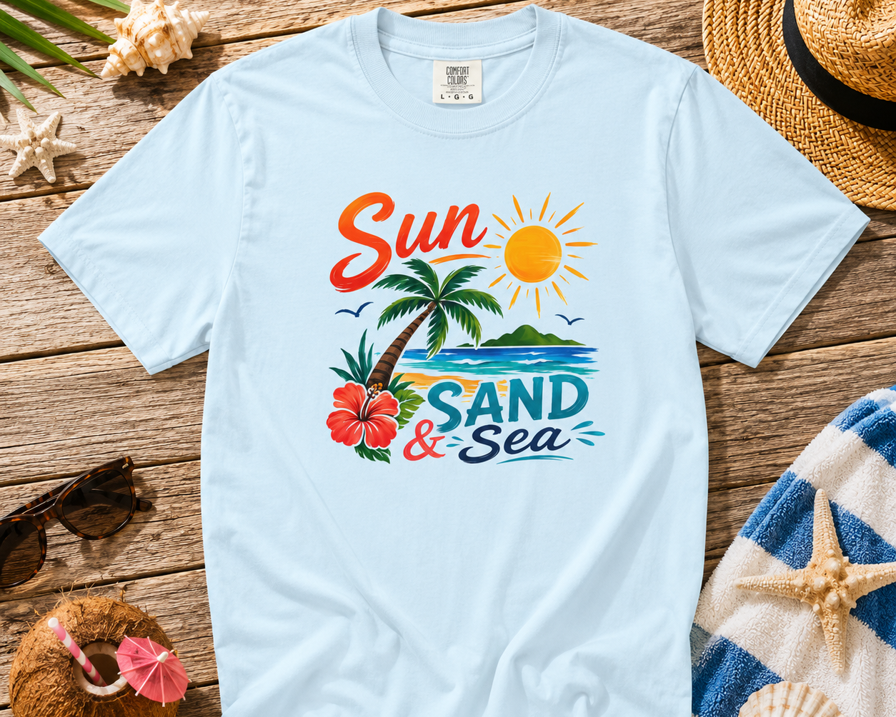 White t-shirt with 'Sun, Sand & Sea' design on a wooden surface with beach-themed accessories.