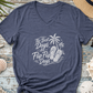 A heather navy blue V-neck t-shirt with a white graphic reading 'The Best Days Are Flip-Flop Days' alongside palm trees and flip-flops, styled in a flat lay on a distressed blue wooden surface surrounded by beach-themed props like a straw hat, sunglasses, starfish, and seashells.
