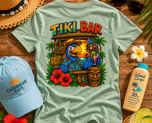 Light green t-shirt with 'Tiki Bar' design on a wooden surface with accessories.