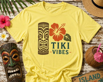 Yellow t-shirt with Tiki Vibes design on a wooden surface with tropical decorations.