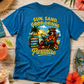 Blue t-shirt with tropical design and text on a wooden surface with beach-themed items.