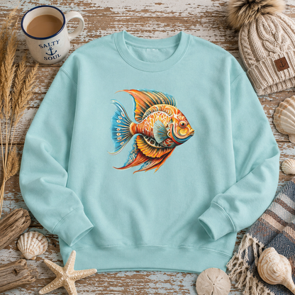 A light aqua crewneck sweatshirt featuring a colorful, detailed illustration of a goldfish on the chest, styled in a flat-lay arrangement with a mug, knit hat, starfish, and seashells on a rustic wooden background.