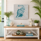 Nautical-themed decor with shell art, books, and plants in a home setting.