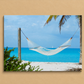 Hammock between two palm trees with a clear blue sky and ocean in the background