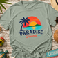 Green t-shirt with 'Paradise Found' design on a wooden surface with beach-themed items.