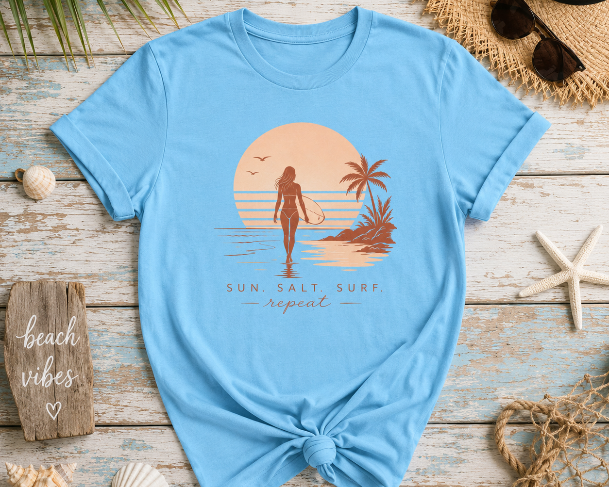 Light blue t-shirt with a beach-themed graphic on a wooden surface with beach accessories.