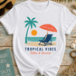White t-shirt with tropical design featuring palm trees, a sun, and beach chair on a wooden surface with beach accessories.